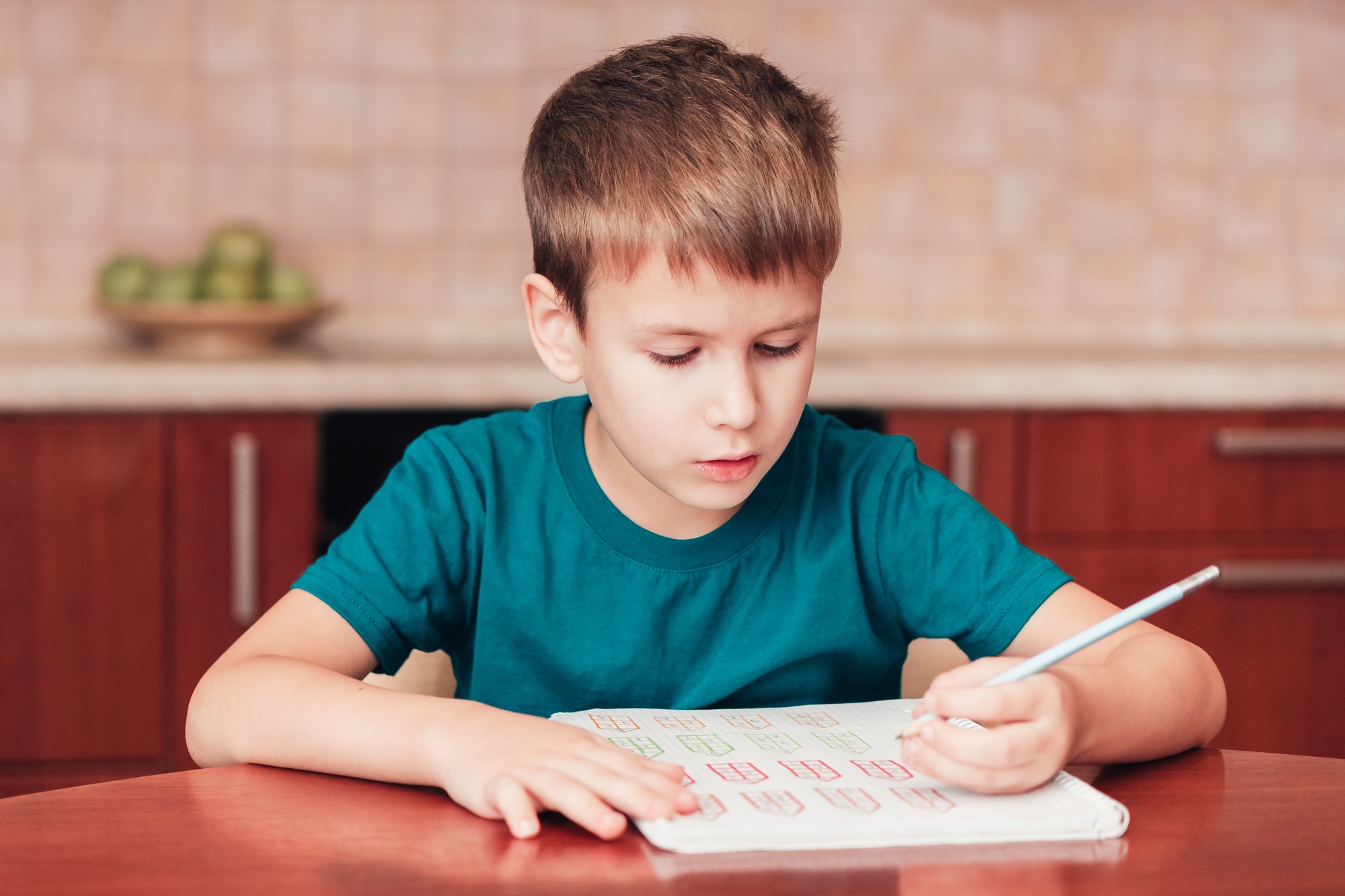 Cute schoolboy learn math at homework sitting by table in kitchen