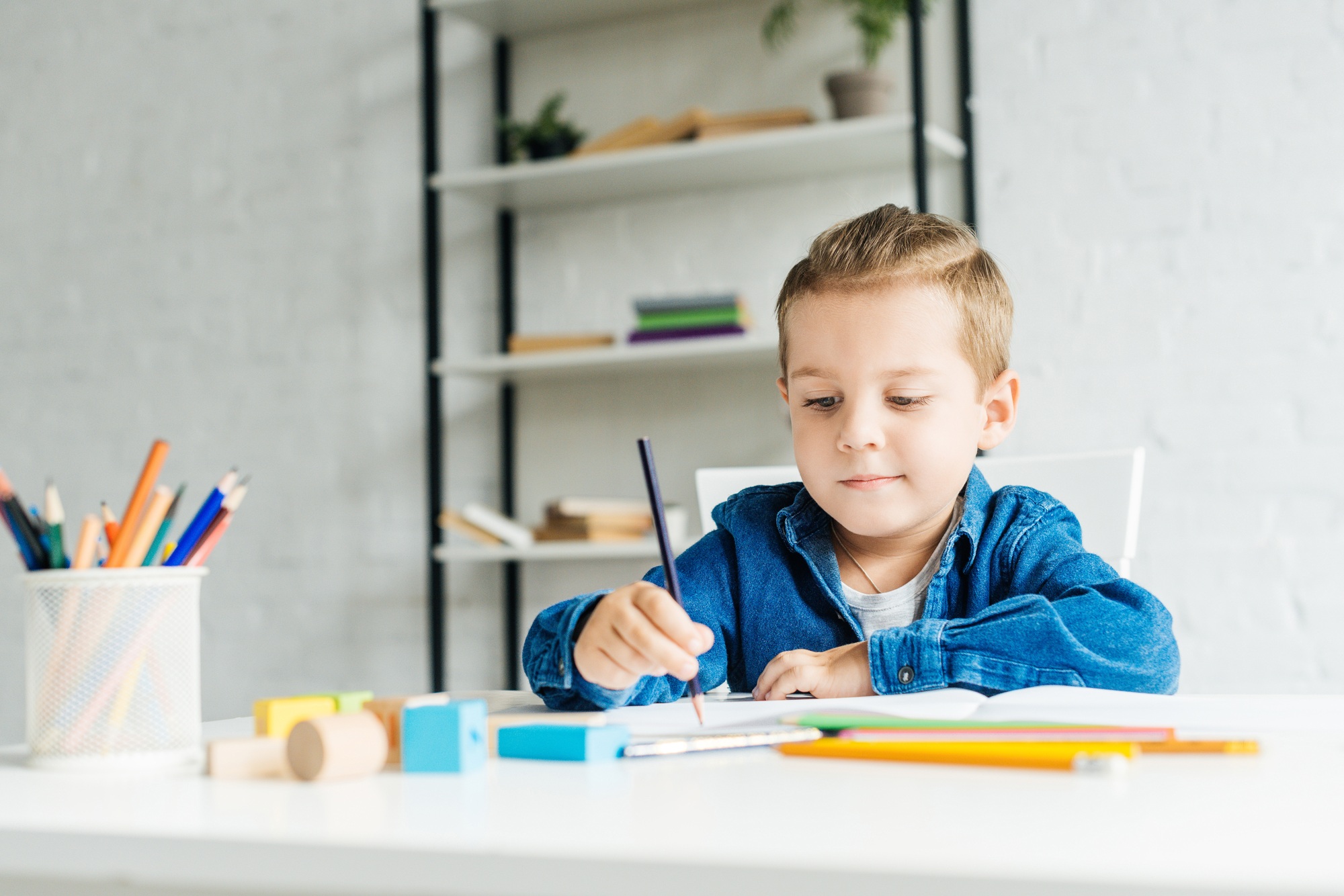 focused little child drawing with color pencils at home