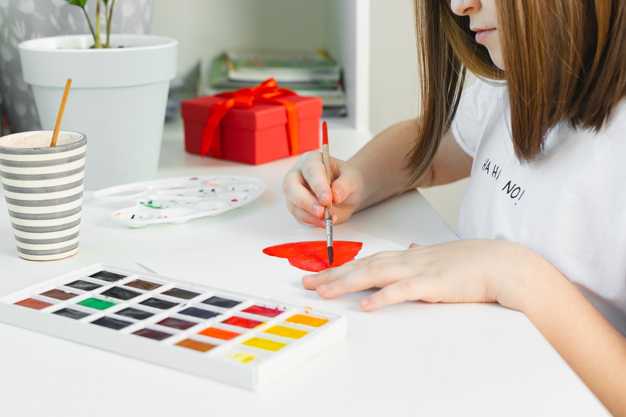 Girl drawing red heart on with watercolors