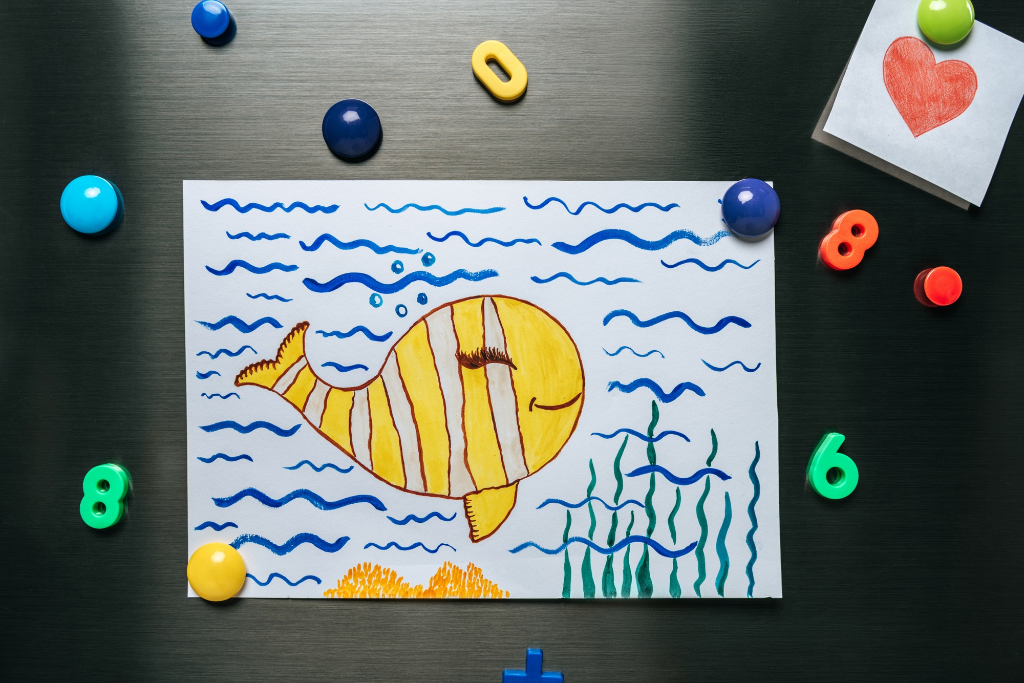 goldfish in ocean picture hanging on stainless steel fridge near heart and magnets