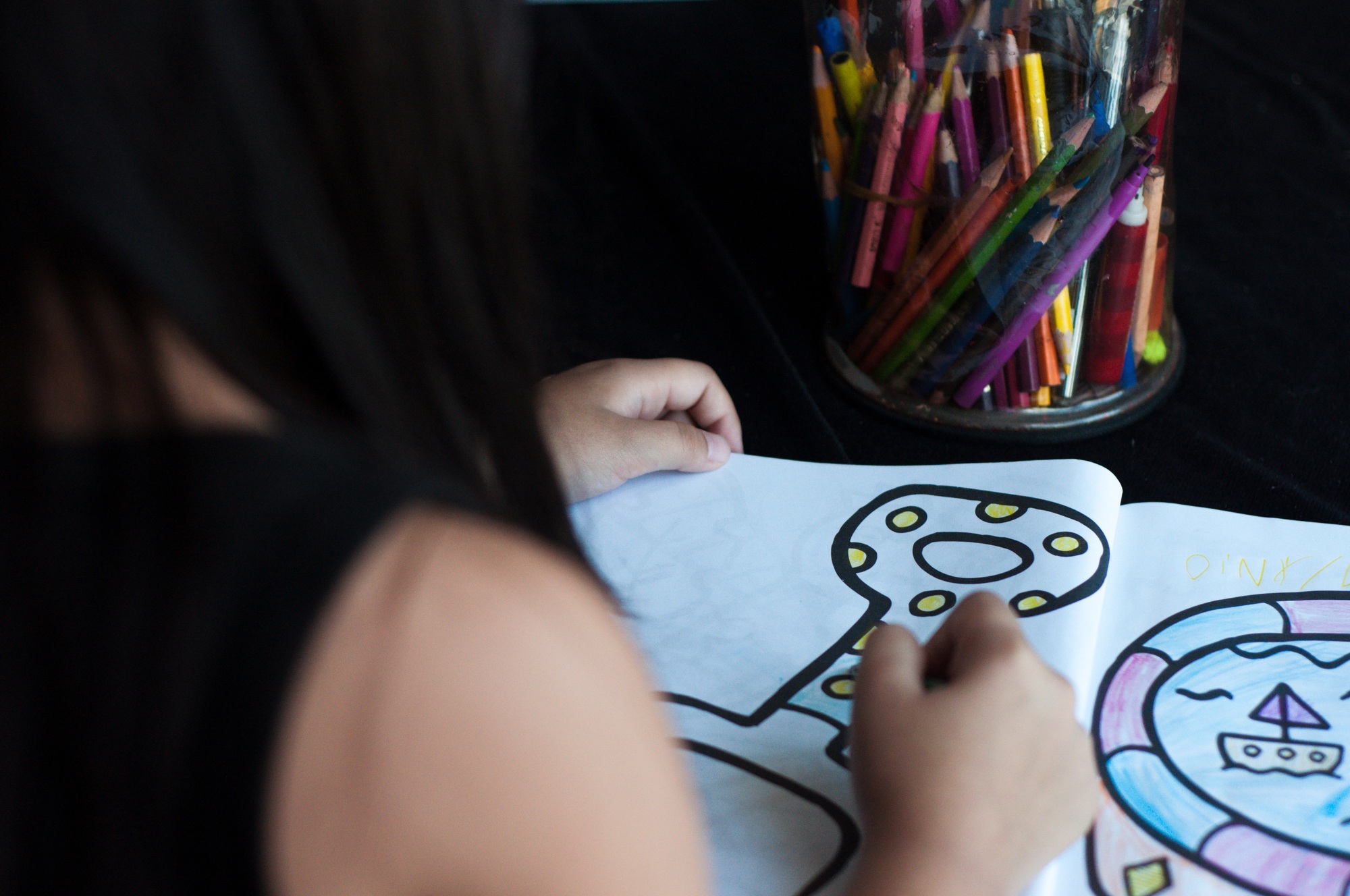 child is colouring a page in the book, view from behind
