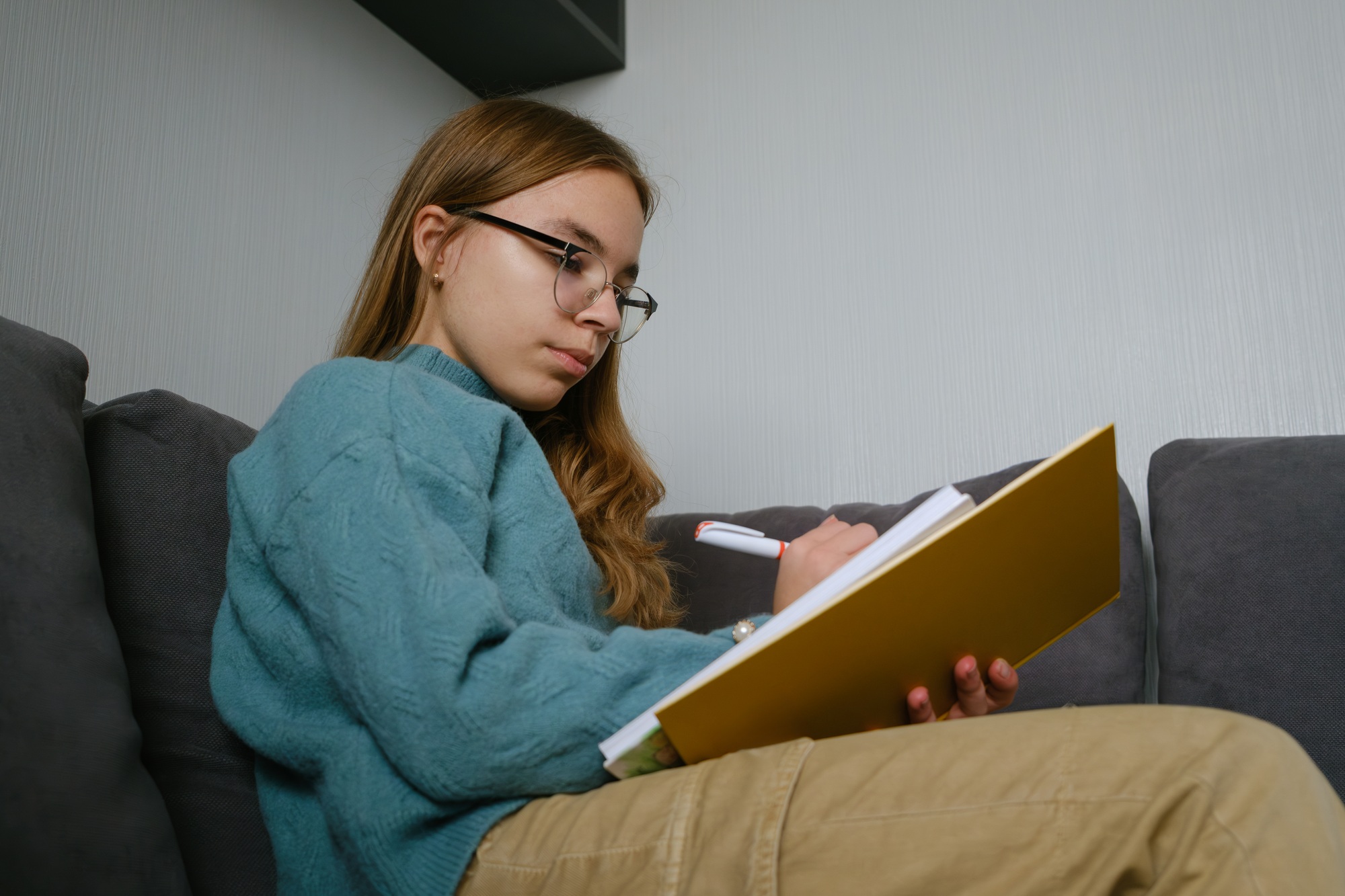 Teenage girl studying while writing notes in notebook at home