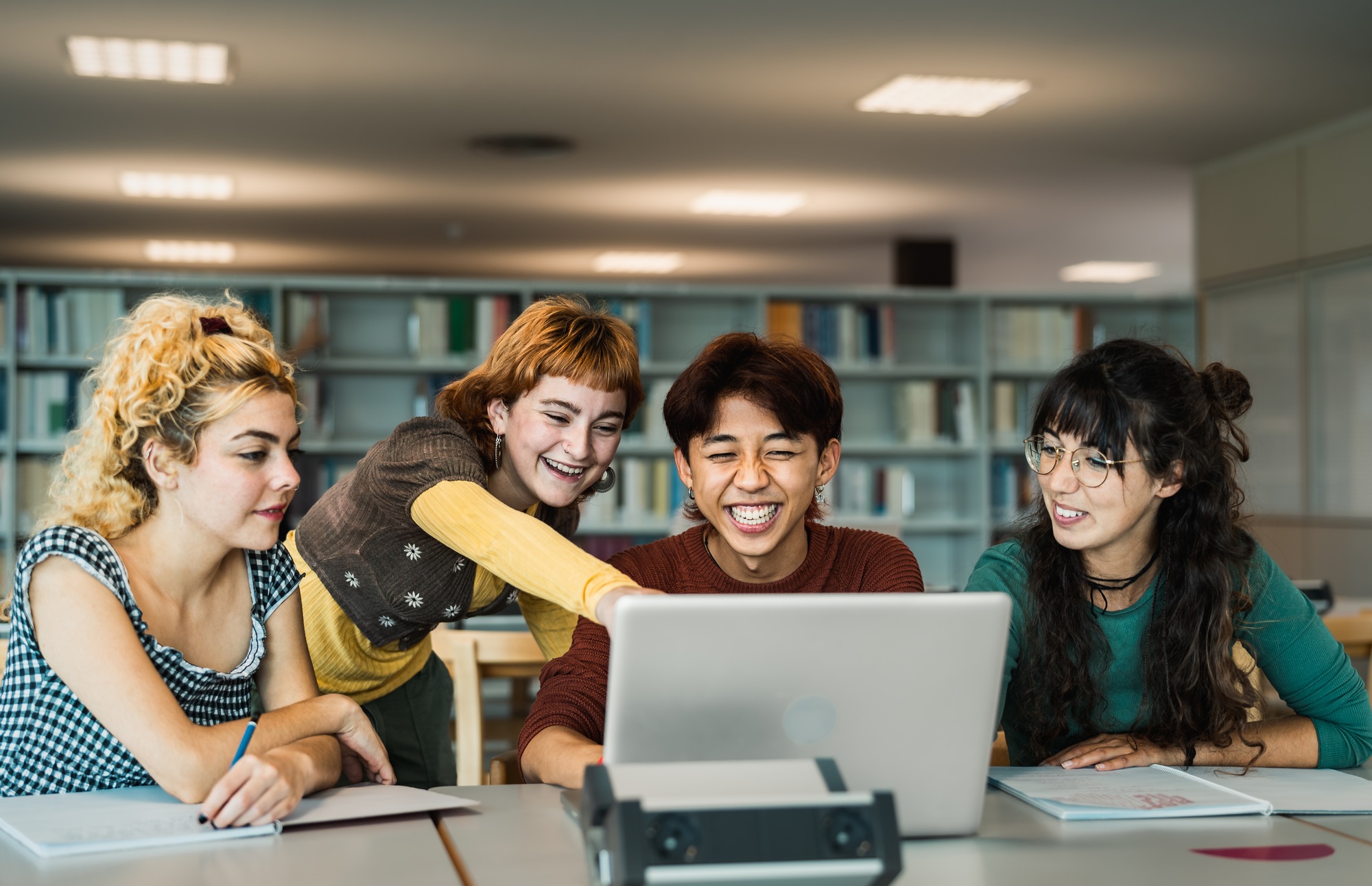 Young university students using laptop and studying with books in library - School education concept